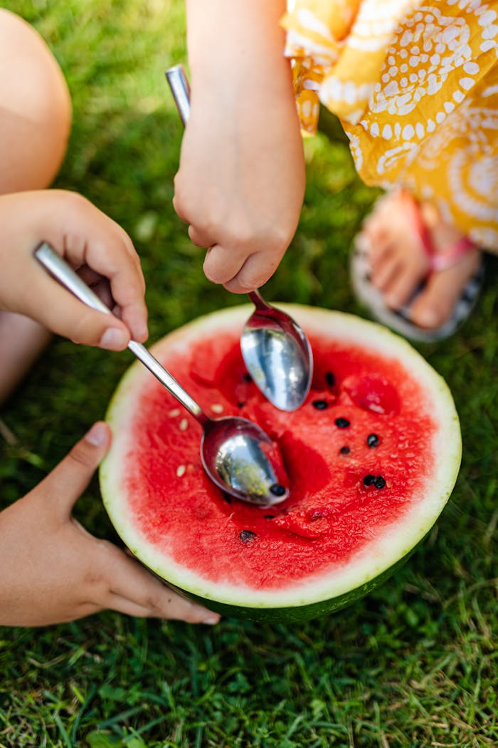 Close-up of kids eating a watermelon with spoons on a sunny day.